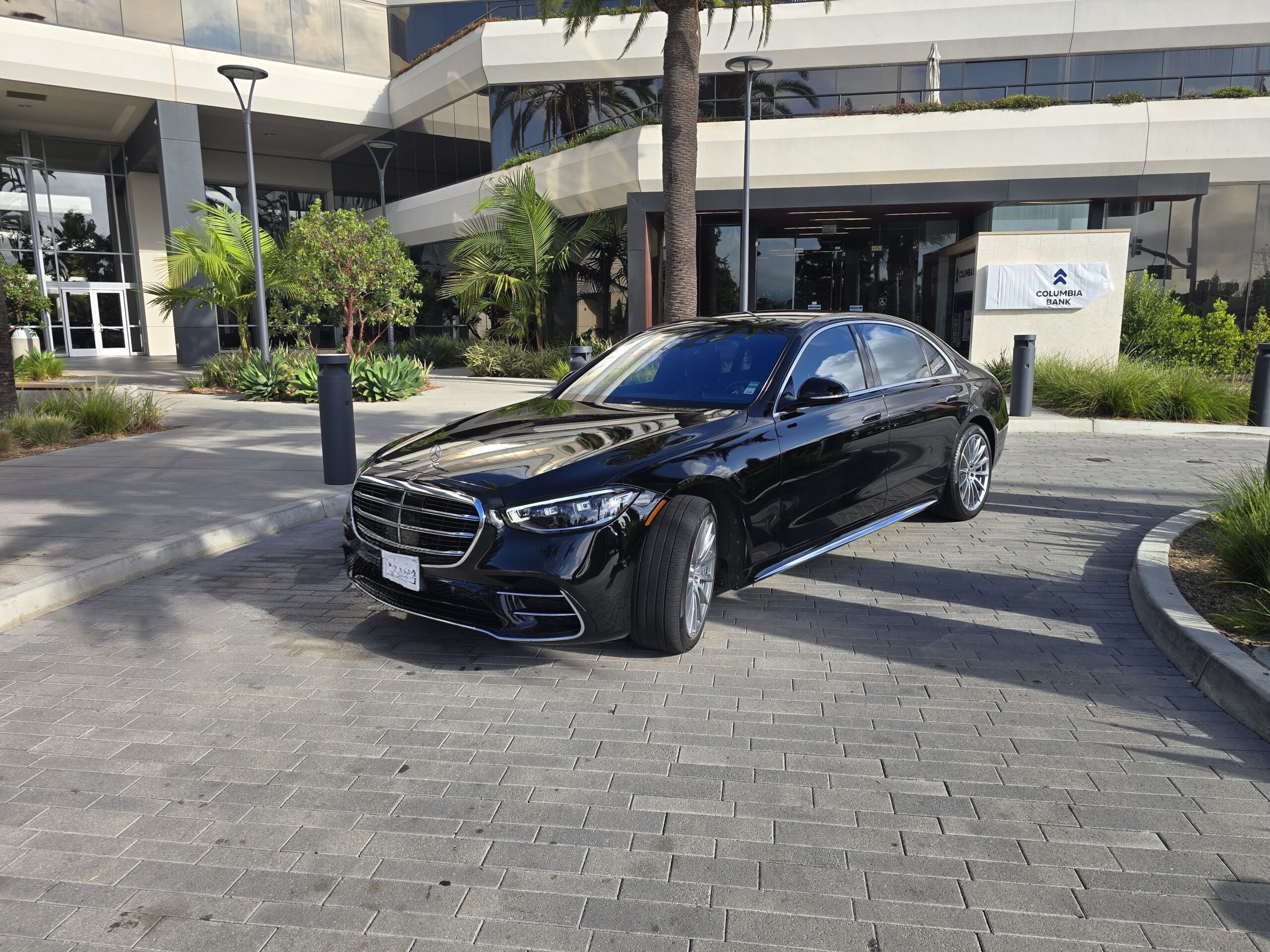 Black Mercedes-Benz S-Class parked outside a modern building with large glass windows, showcasing luxury automotive design.