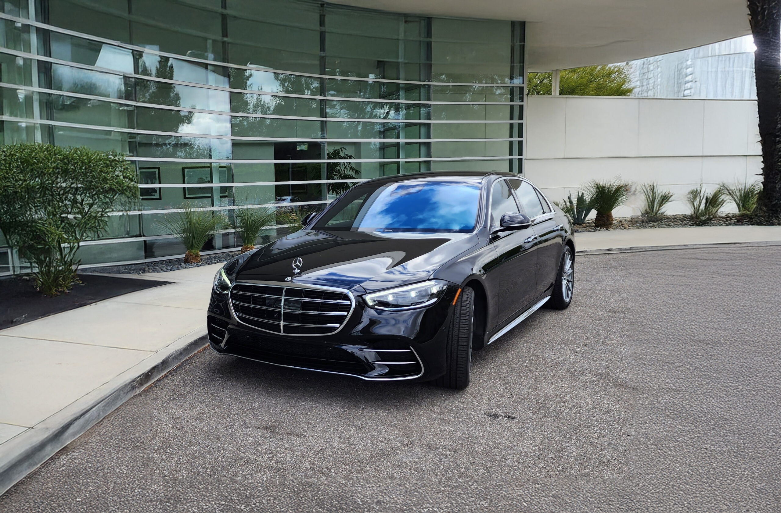 Black Mercedes-Benz S-Class parked outside a modern building with large glass windows, showcasing luxury automotive design.