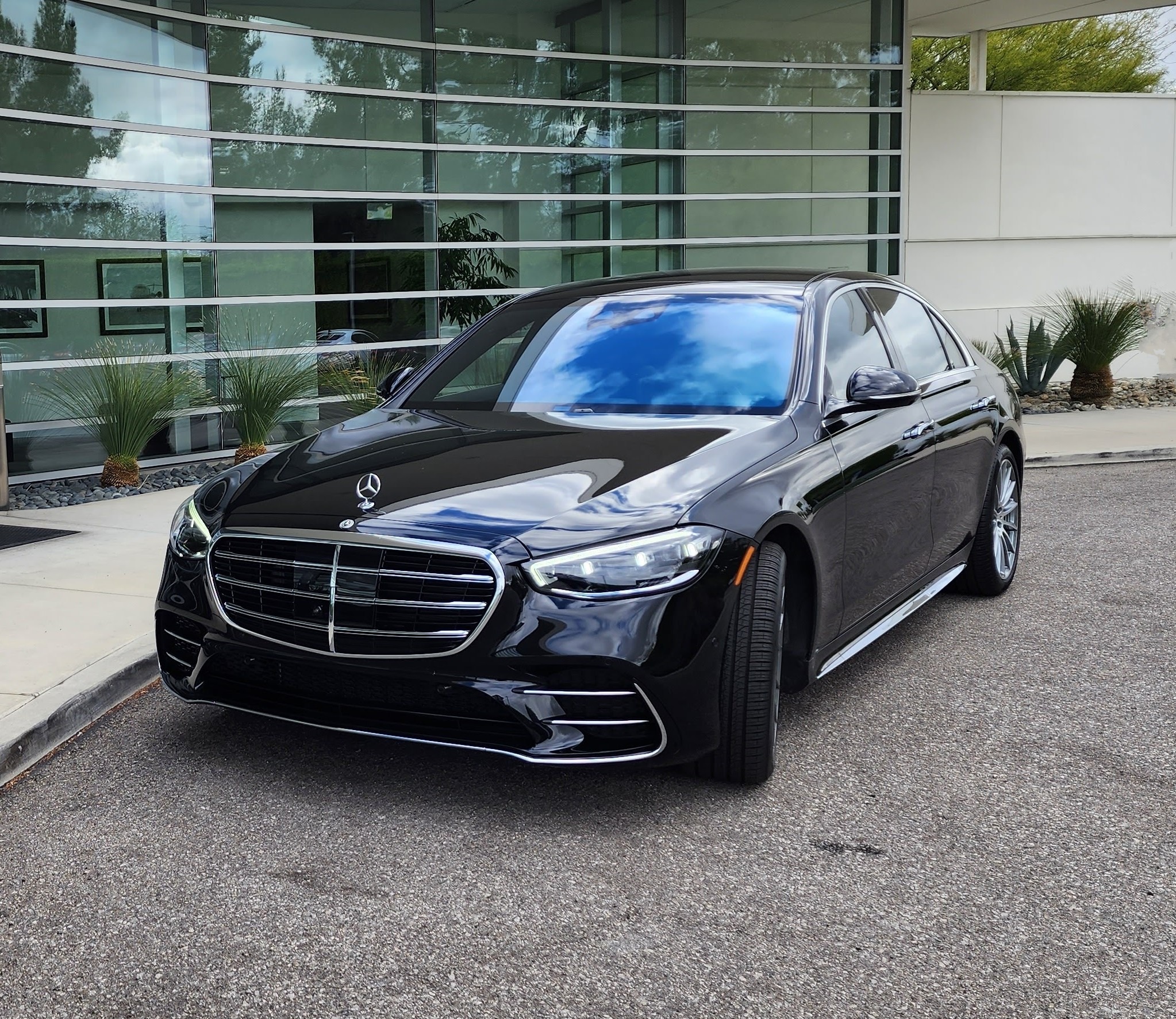 A sleek black Mercedes-Benz luxury sedan parked in front of a modern glass building, showcasing its elegant design and premium features.