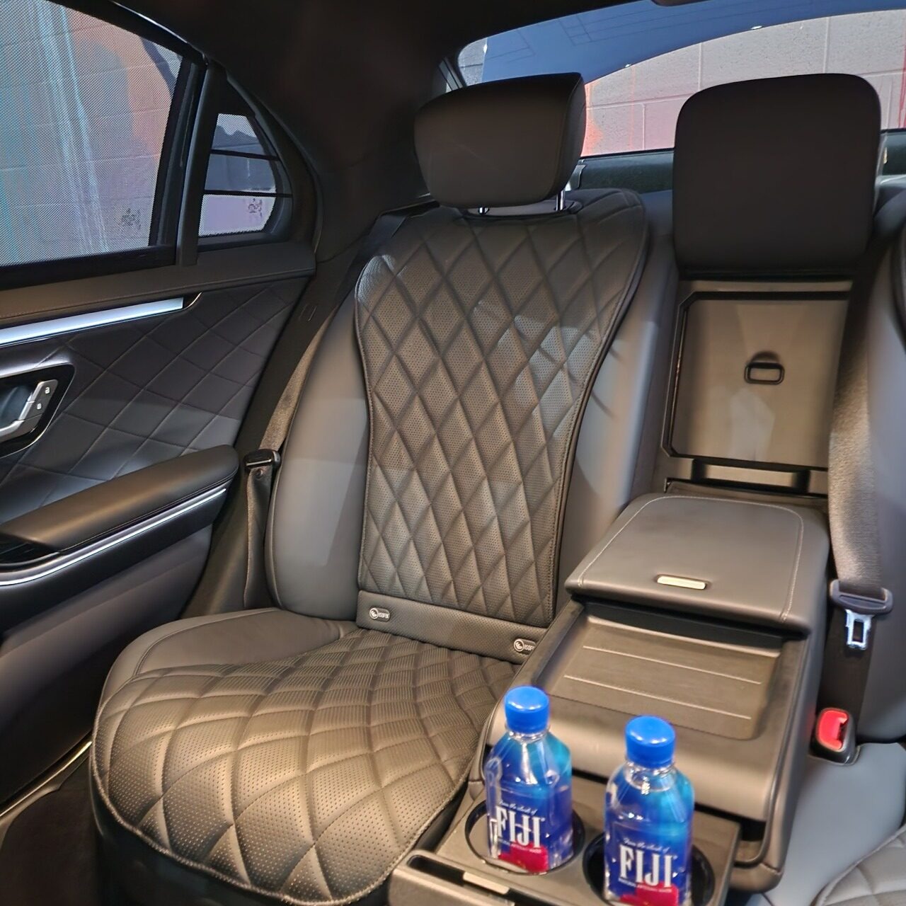 Luxurious black leather backseat of a vehicle featuring diamond-patterned upholstery, complemented by two bottled waters in cup holders.