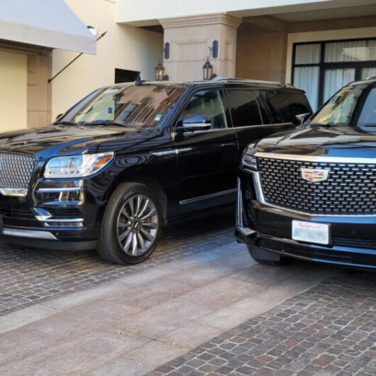 Two luxury SUVs, a Lincoln and a Cadillac, parked outside a hotel entrance, showcasing their sleek designs against the building’s elegant backdrop.