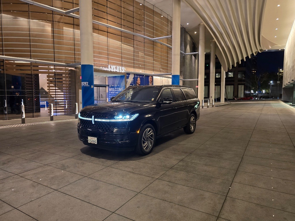 Black luxury SUV parked in an illuminated entrance area, showcasing modern architecture. Highlights elegance and urban nightlife.